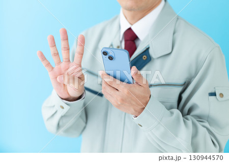 スマホを持って指を4本立てる作業着姿のミドル男性ビジネスマン 130944570