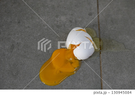 Eggshell cracks open on a cold, gray surface revealing bright golden yolk in daylight Eggshell cracks open on a cold, gray surface revealing bright golden yolk in daylight 130945084