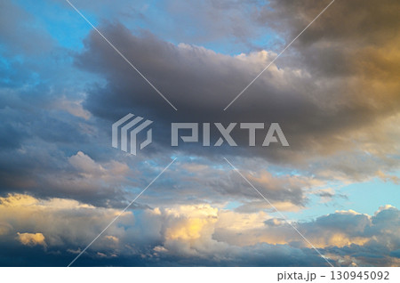 Shifting clouds dance across the vibrant sky at sunset, painting the horizon 130945092