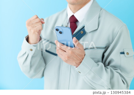 スマホを持ってガッツポーズする作業着姿のミドル男性ビジネスマン スマホを持ってガッツポーズする作業着姿のミドル男性ビジネスマン 130945384