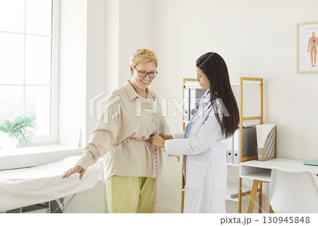 Young doctor, nurse woman holding measurement tape to measure senior patient waist to check 130945848