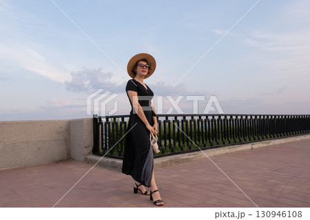 Elegant woman in polka dot dress stands on promenade 130946108