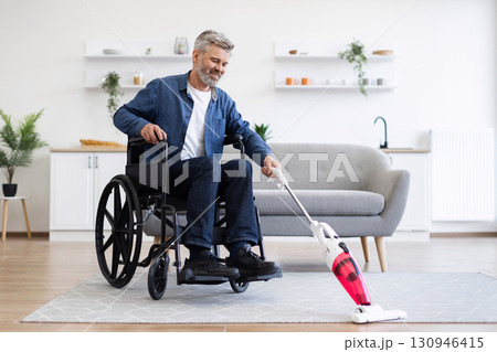 Middle-aged man using wheelchair holding vacuum cleaner, participating in household cleaning activities, modern room setting Middle-aged man using wheelchair holding vacuum cleaner, participating in household cleaning activities, modern room setting 130946415