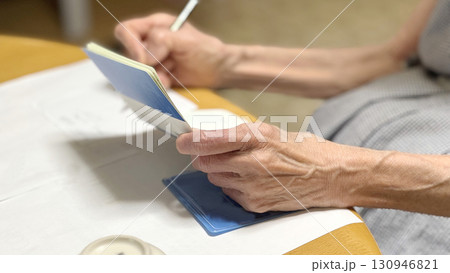 通帳を開いて書き込む高齢女性の手 通帳を開いて書き込む高齢女性の手 130946821