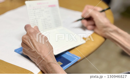 通帳を開いてメモに書き込む高齢女性の手元 130946827