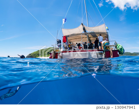 カタマランヨットのダイビングクルーズ船の半水面撮影。美しいサンゴ礁と熱帯魚の群れ。 沖縄県島尻郡慶良 130947941