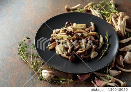 Fried shimeji mushrooms with thyme and garlic on a black plate. Fried shimeji mushrooms with thyme and garlic on a black plate. 130948080