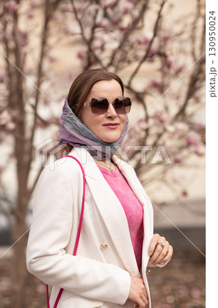 Woman Magnolia Flowers Spring Woman in scarf, sunglasses, white blazer poses near magnolia tree in spring for fashion. 130950024