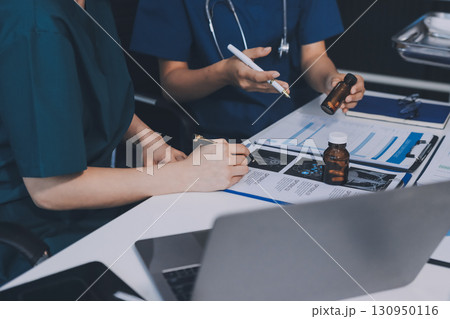 Two doctors and a female nurse meet at a table in the hospital, collaborating on medical tasks using laptops and computers 130950116
