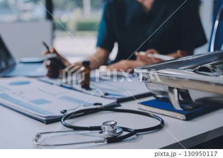 Two doctors and a female nurse meet at a table in the hospital, collaborating on medical tasks using laptops and computers Two doctors and a female nurse meet at a table in the hospital, collaborating on medical tasks using laptops and computers 130950117