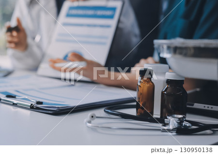 Medical team meeting analyzing blood test results in hospital laboratory. Doctors and scientists in lab coats are having a discussion about blood test result, holding test tubes and taking notes. 130950138