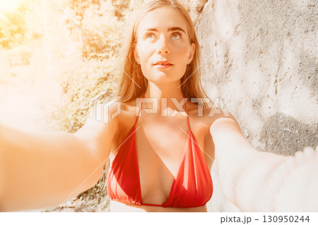Woman Beach Selfie Summer - A woman in a red bikini takes a selfie on a beach with bright sunlight. 130950244