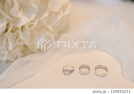 Wedding rings and engagement ring displayed with white hydrangeas and veil, symbolizing love, commitment, celebration of marriage 130950251