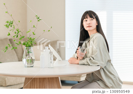 朝,リビングでグラスに注いだミネラルウォーター,水,白湯を飲む若いアジア人,日本人女性(デトックス) 130950549