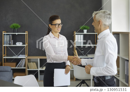 Friendly male and female business partners shake hands to confirm their partnership. Friendly male and female business partners shake hands to confirm their partnership. 130951531
