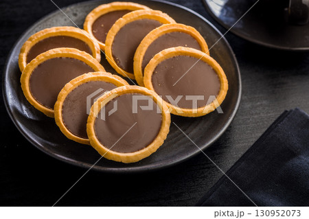 Sweet chocolate tartelettes on plate on black table. Sweet chocolate tartelettes on plate on black table. 130952073