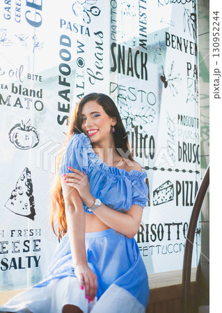 Woman in blue outfit posing happily by restaurant menu window in bright daylight Woman in blue outfit posing happily by restaurant menu window in bright daylight 130952244