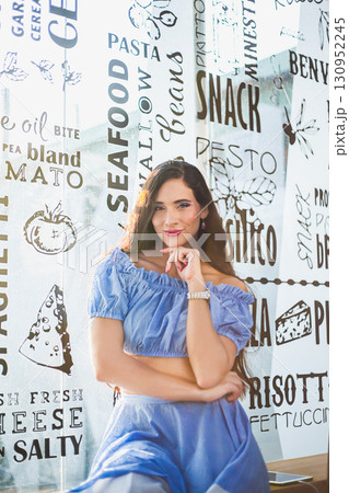 Woman in blue dress poses in a trendy restaurant with a unique wall design Woman in blue dress poses in a trendy restaurant with a unique wall design 130952245