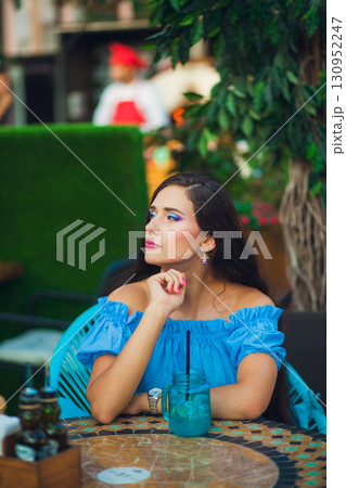 Young woman with colorful makeup enjoys a drink at a vibrant outdoor cafe in warm weather Young woman with colorful makeup enjoys a drink at a vibrant outdoor cafe in warm weather 130952247