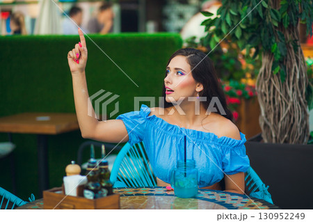 Woman signaling waiter at a lively street restaurant during a sunny day 130952249