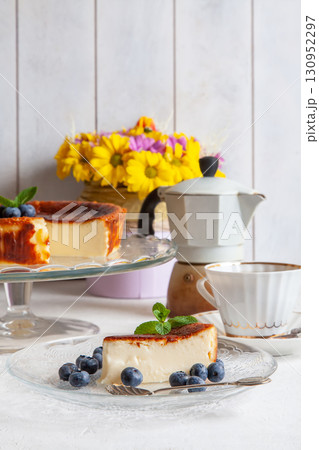 Slice of Homemade Basque burnt cheesecake on a plate with blueberries and mint leaves on light background, cup of coffee, geyser coffee maker, bouquet of yellow flowers Slice of Homemade Basque burnt cheesecake on a plate with blueberries and mint leaves on light background, cup of coffee, geyser coffee maker, bouquet of yellow flowers 130952297