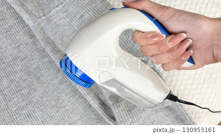 A woman holds a lint remover against a gray warm sweater with bobbles, removing pilling and caring for clothes. Preparing wardrobe for winter and autumn seasons, clothing care and maintenance 130953161
