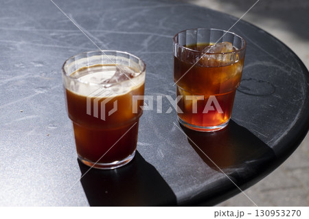 Two glasses of coffee iced americano and cold brew on a black table outside, showcasing rich colors and textures, with sunlight casting soft shadows, creating a refreshing beverage scene 130953270