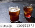 Two glasses of iced coffee with ice cubes, placed on a dark table, showcasing refreshing beverages in bright sunlight, perfect for summer enjoyment and relaxation 130953272