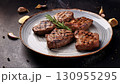 Grilled beef steaks with rosemary, salt, and pepper on wooden board. Juicy barbecue meat with spices. Delicious cooked beef fillet on dark rustic background. 130955295