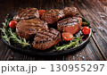 Grilled beef steaks with rosemary, salt, and pepper on wooden board. Juicy barbecue meat with spices. Delicious cooked beef fillet on dark rustic background. 130955297
