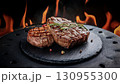 Grilled beef steaks with rosemary, salt, and pepper on wooden board. Juicy barbecue meat with spices. Delicious cooked beef fillet on dark rustic background. 130955300