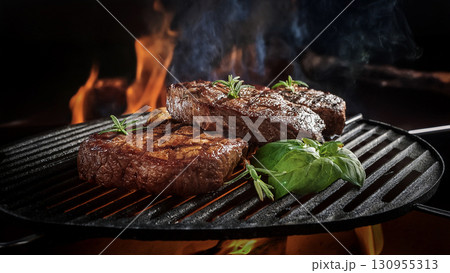 Grilled beef steaks with rosemary, salt, and pepper on wooden board. Juicy barbecue meat with spices. Delicious cooked beef fillet on dark rustic background. 130955313