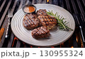 Grilled beef steaks with rosemary, salt, and pepper on wooden board. Juicy barbecue meat with spices. Delicious cooked beef fillet on dark rustic background. 130955324