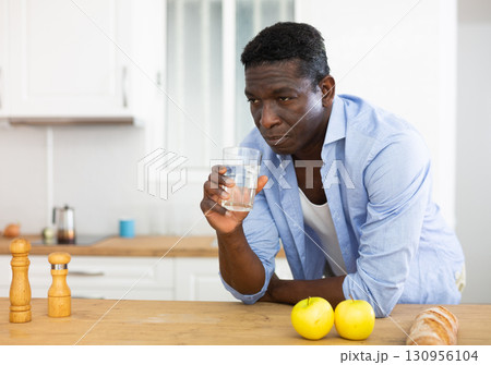 man drinks water after preparing a vegetable salad in the kitchen man drinks water after preparing a vegetable salad in the kitchen 130956104