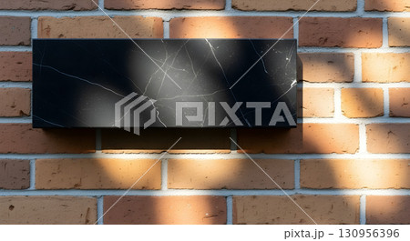 A black marble sign with veins is mounted on a brick wall, bathed in sunlight. 130956396