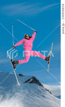 Skier in pink suit performing aerial split jump with joyful energy over snowy mountain. Hand made collage Skier in pink suit performing aerial split jump with joyful energy over snowy mountain. Hand made collage 130956634