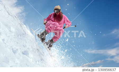 Female skier in pink outfit carving snowy slope with spray of snow under bright blue sky. Hand made collage 130956637