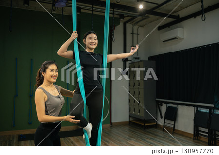 Personal trainer helping woman perform aerial yoga pose, healthy lifestyle and fitness concept 130957770