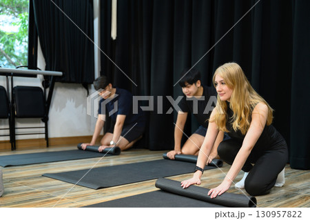 Group of young adults rolling up yoga mats after a fitness or yoga class in a modern studio 130957822