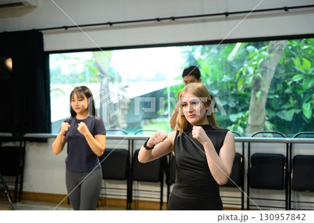 Fitness instructor leading boxing workout with students following punching exercises Fitness instructor leading boxing workout with students following punching exercises 130957842