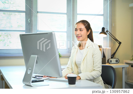 Confident female entrepreneur focused on online tasks in a bright office workspace. 130957862