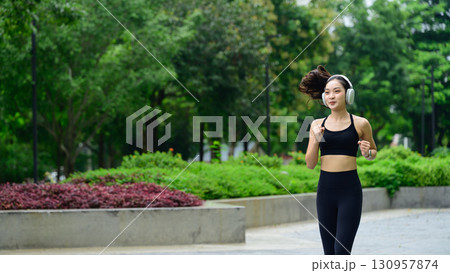Young woman jogging outdoors in a park while listening to music with wireless headphones Young woman jogging outdoors in a park while listening to music with wireless headphones 130957874