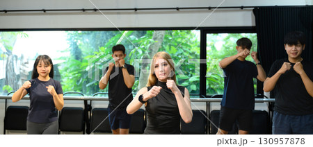 Group of young adults practicing boxing moves together in a bright indoor fitness studio 130957878