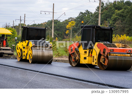 Two asphalt rollers compacting fresh pavement during road construction project Two asphalt rollers compacting fresh pavement during road construction project 130957995