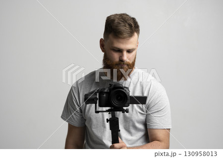 Bearded man holding professional camera on stabilizer for filmmaking and video work 130958013