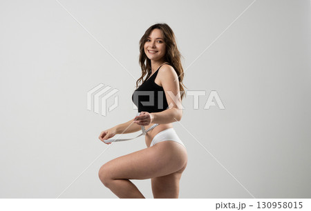 Smiling young woman measuring waist with tape in underwear for fitness and health 130958015