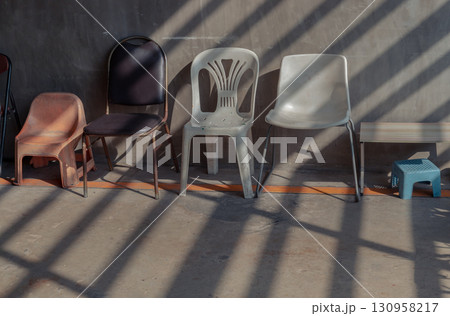View of Different of Chairs with Morning sunlight shines through Wooden battens front of Old cement wall. View of Different of Chairs with Morning sunlight shines through Wooden battens front of Old cement wall. 130958217