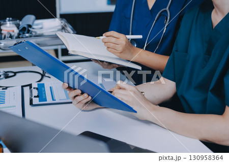 Two doctors and a female nurse meet at a table in the hospital, collaborating on medical tasks using laptops and computers Two doctors and a female nurse meet at a table in the hospital, collaborating on medical tasks using laptops and computers 130958364