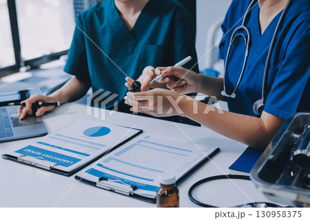 Medical team meeting analyzing blood test results in hospital laboratory. Doctors and scientists in lab coats are having a discussion about blood test result, holding test tubes and taking notes. 130958375