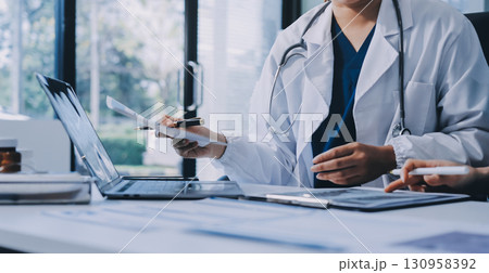 Medical team meeting analyzing blood test results in hospital laboratory. Doctors and scientists in lab coats are having a discussion about blood test result, holding test tubes and taking notes. 130958392